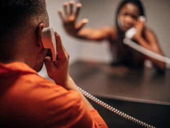 Incarcerated black male talking to spouse on prison phone.